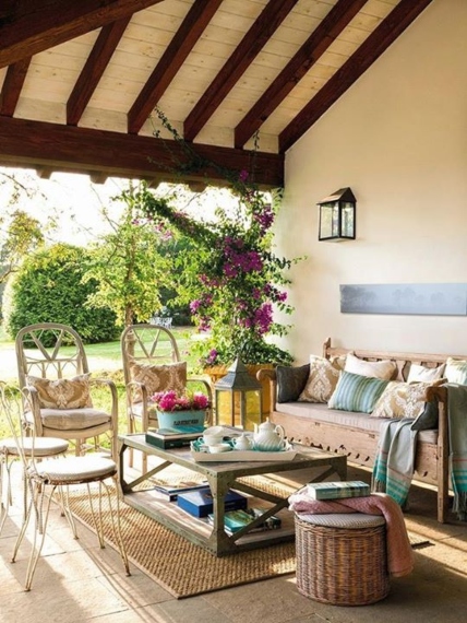 Quintal de uma casa decorado com sofá, mesa de centro e tapete na cor bege, juntamente de almofadas em tons pastéis